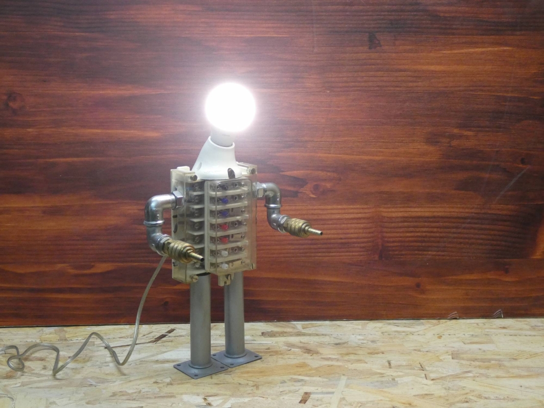 Escultura lámpara robot realizada con material reciclado, antiguo conector eléctrico y piezas de fontanería y aire comprimido. MEDIDAS: Ancho 43 cm X Alto 23 cm 
