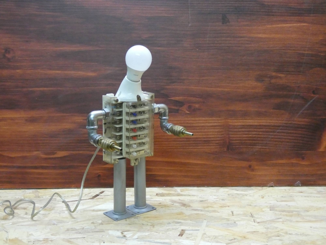 Escultura lámpara robot realizada con material reciclado, antiguo conector eléctrico y piezas de fontanería y aire comprimido. MEDIDAS: Ancho 43 cm X Alto 23 cm 